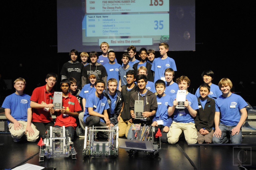 Students on stage holding VEX trophies behind three robots